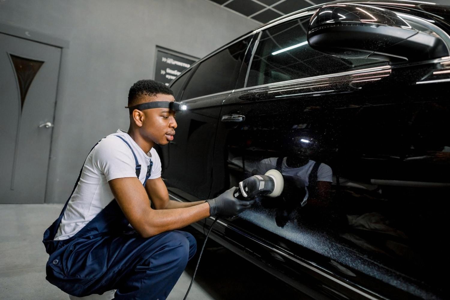 Technician using a dual-action polisher to remove small scratches from a black car in a Dubai detailing studio