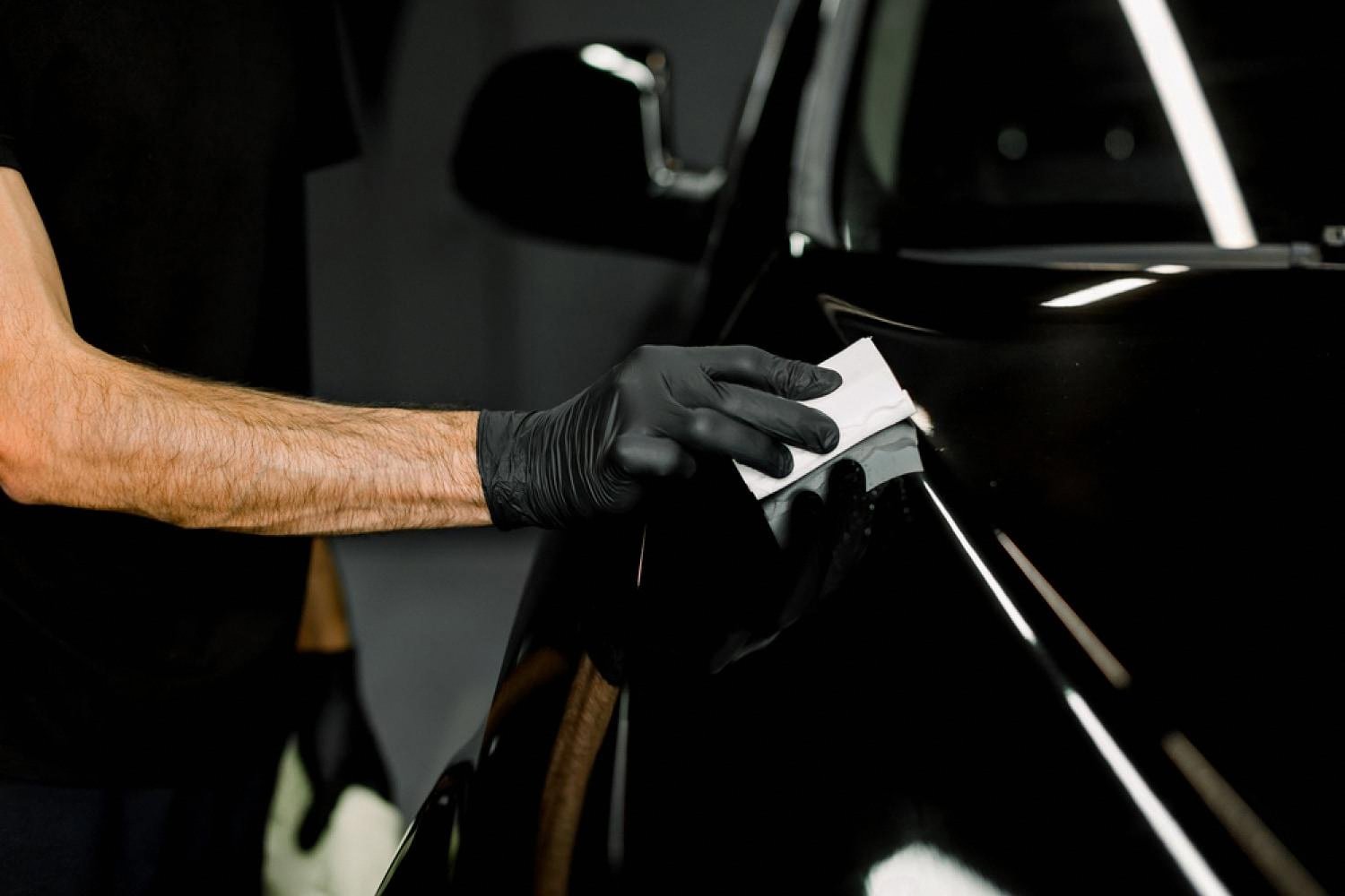 Detailer in black gloves applying ceramic coating to a black car body to protect against scratches